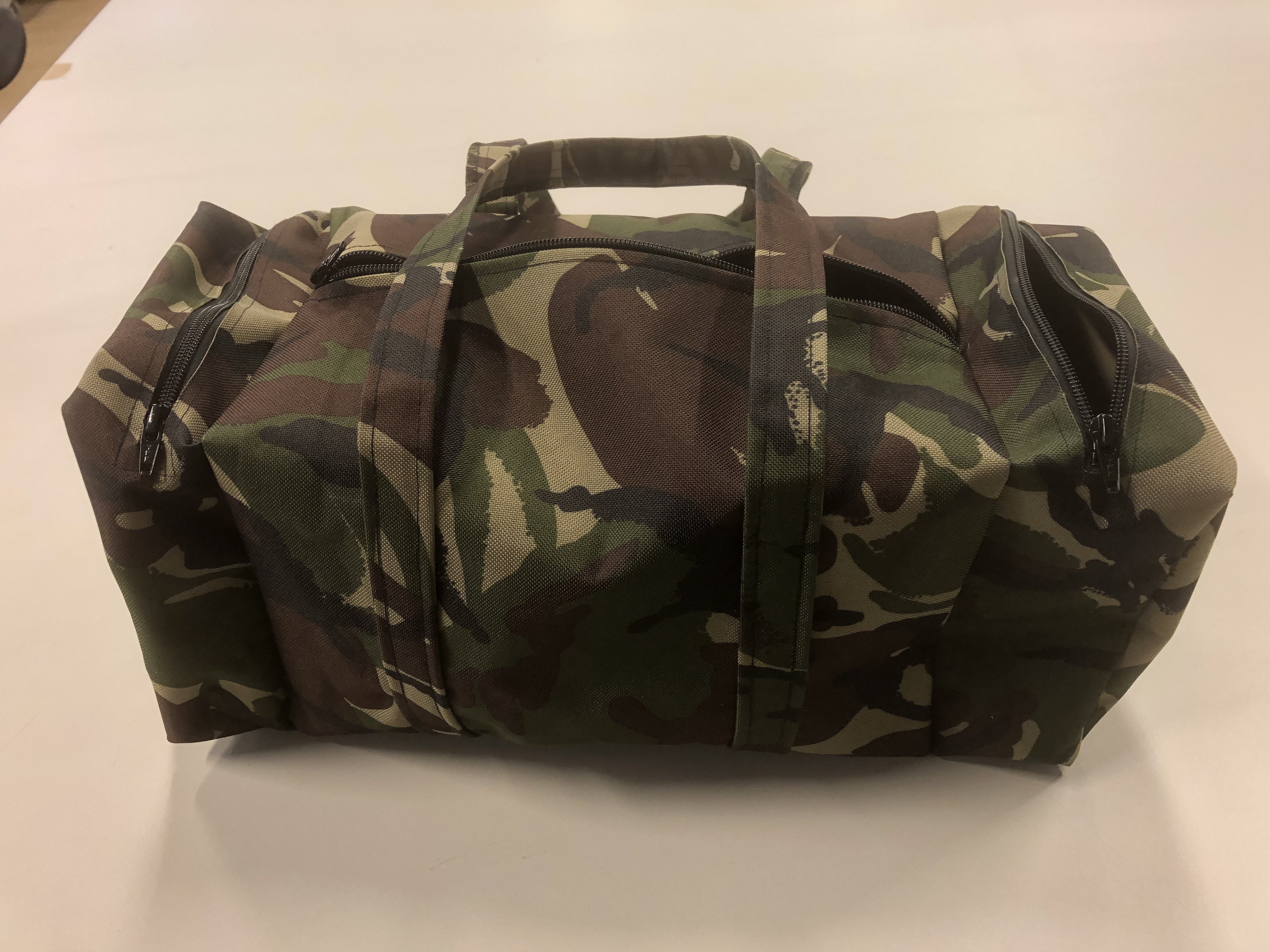 Camouflage duffelv&auml;ska med dragkedjor, placerad p&aring; en vit yta.